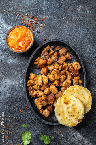 COLOMBIAN FOOD. Fried pork CHICHARRON, AREPAS and colombian tomato sauce. Top view. Black background