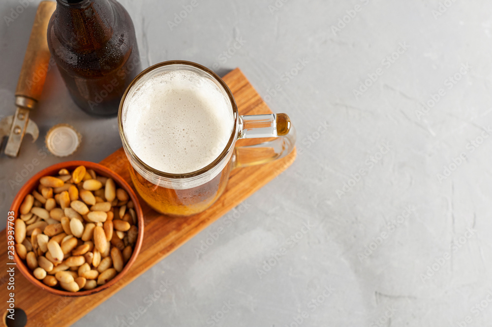 Lager beer pouring in glass and bottle with salted peanuts on gray concrete background Lager beer pouring in glass and bottle with salted peanuts on gray concrete background