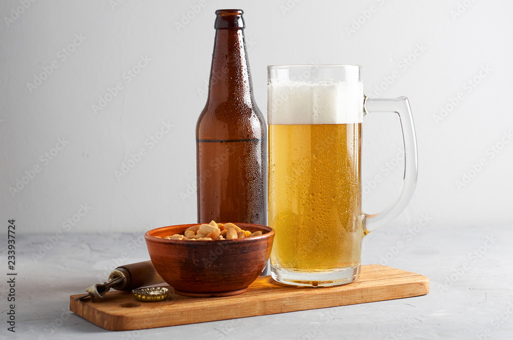 Lager beer pouring in glass and bottle with salted peanuts on gray concrete background