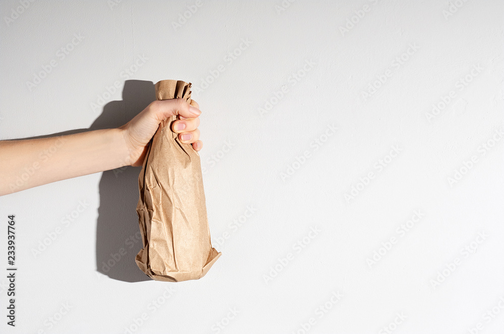 Hand holding beer bottle in the paper bag on gray concrete background