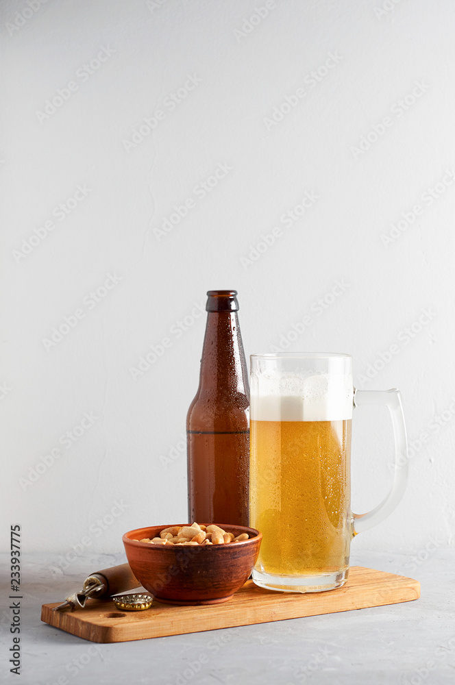 Lager beer pouring in glass and bottle with salted peanuts on gray concrete background