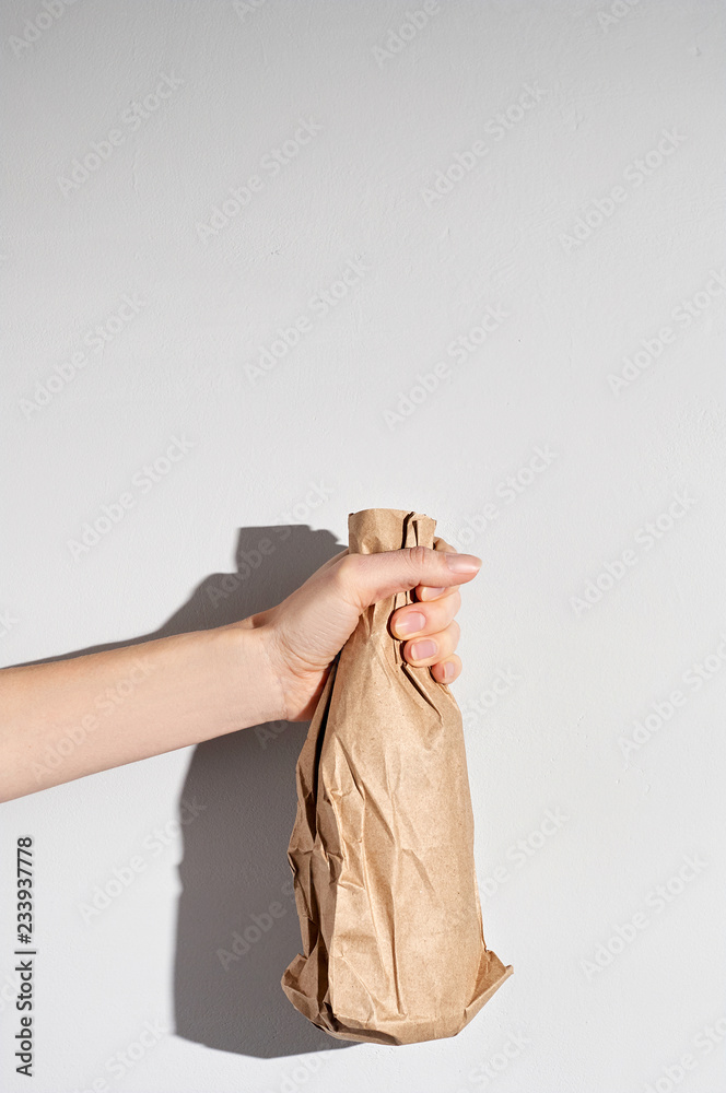 Hand holding beer bottle in the paper bag on gray concrete background