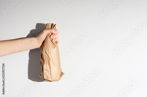 Obraz na płótnie Hand holding beer bottle in the paper bag on gray concrete background w salonie
