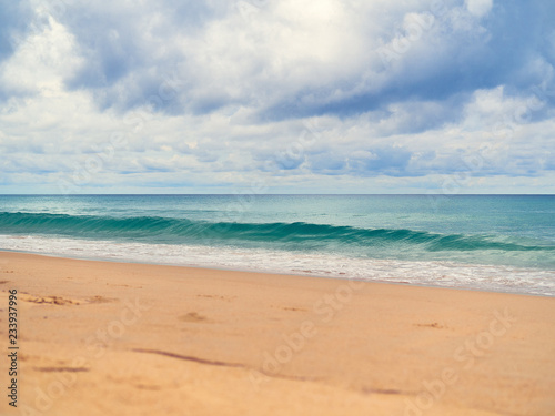 View of the paradise beach with golden sand, waves on the sea and the sky with clouds