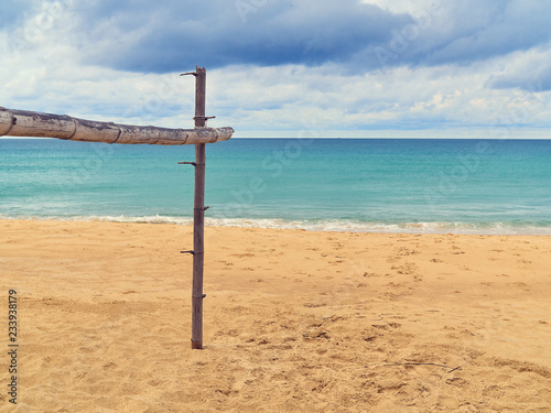 The wooden crossbar is located on a tropical beach. In the distance you can see the sea or the ocean and the sky with clouds.