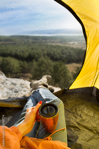 View from the tent. Traveler holds thermocup.
