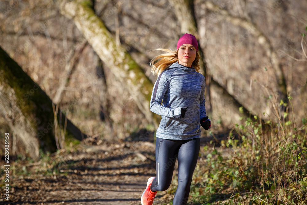Naklejka premium Young woman jogging on trail in autumn park