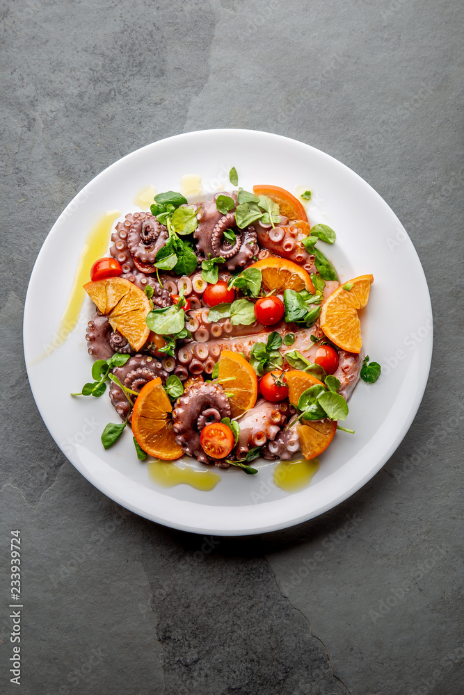 Whole octopus salad with orange, tomatoes and cress salad on white plate. Top view Whole octopus salad with orange, tomatoes and cress salad on white plate. Top view