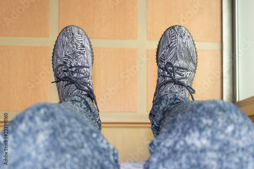 Feet of man who is wearing the gray shoes with stripes pattern above the floor
