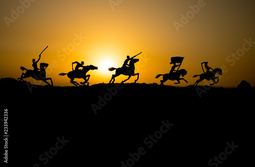 Attacking scene. War concept. Riders on horse ready to fight and soldiers on a dark foggy toned sunset background. Battle scene battlefield of fighting soldiers.