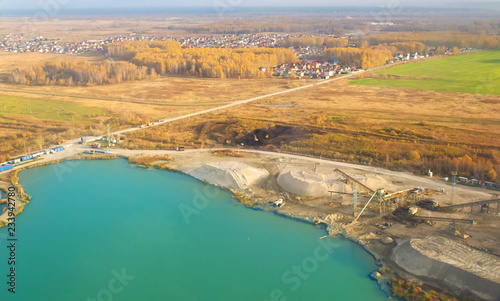 aerial view of a sand mining quarry on a turquoise lake with posted construction equipment and excavators