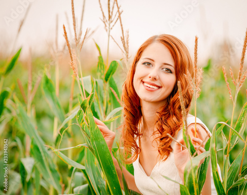 Style redhead girl in white dress is standing in a field of corn cobs at countryside.