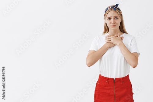 Good-looking silly and stylish woman with fair hair feeling touched and sad guy confessed in love, holding palms on chest and smiling with gloomy expression, cannot answear on feelings photo