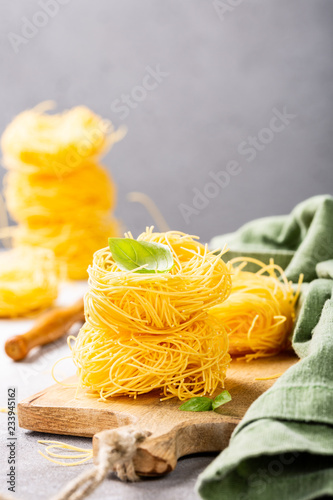 Fresh egg pasta tagliatelle nest on wooden cutting board with basil leaf. Healthy italian food concept with copy space.