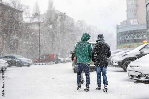 People walking through city street covered with snow during heavy snowfall. Blizzard in town at winter. Natural disasters, snow storm