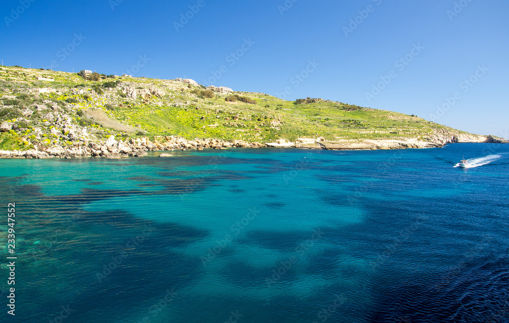 Blue water and sailing motor boat near town Mgarr, Gozo island, Malta