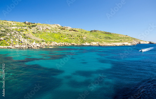 Blue water and sailing motor boat near town Mgarr, Gozo island, Malta