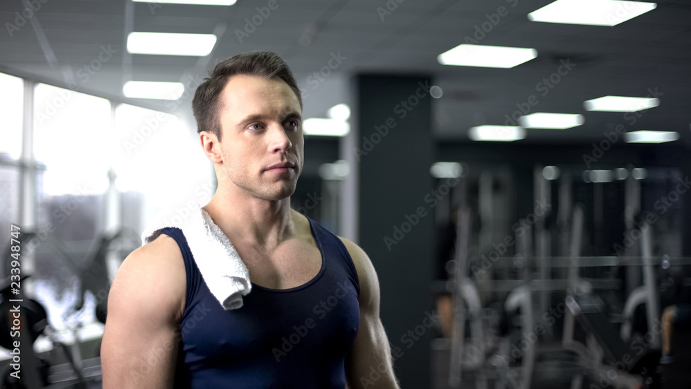 Tired bodybuilder with towel on shoulder relaxing after hard workout in gym Tired bodybuilder with towel on shoulder relaxing after hard workout in gym