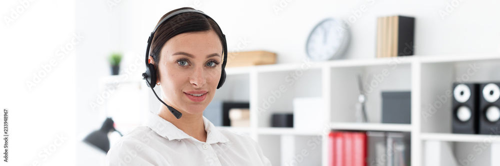 A young girl in headphones with a microphone is in a bright office.