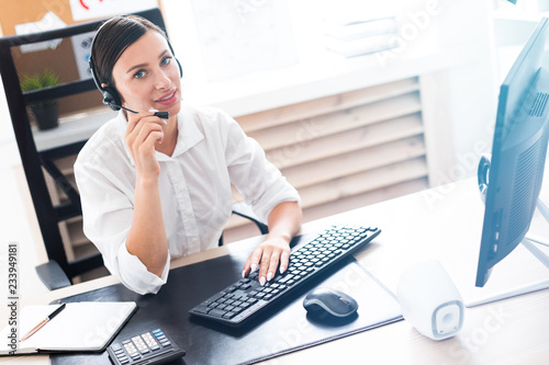 A young girl in headphones with a microphone sitting at a computer table.