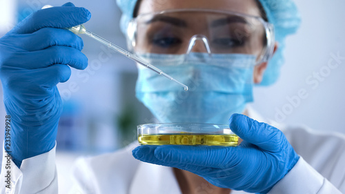 Canvas Print Female lab researcher dripping test liquid in petri dish and checking reaction