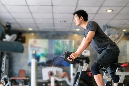 Asian man exercising on stationary bike at gym.