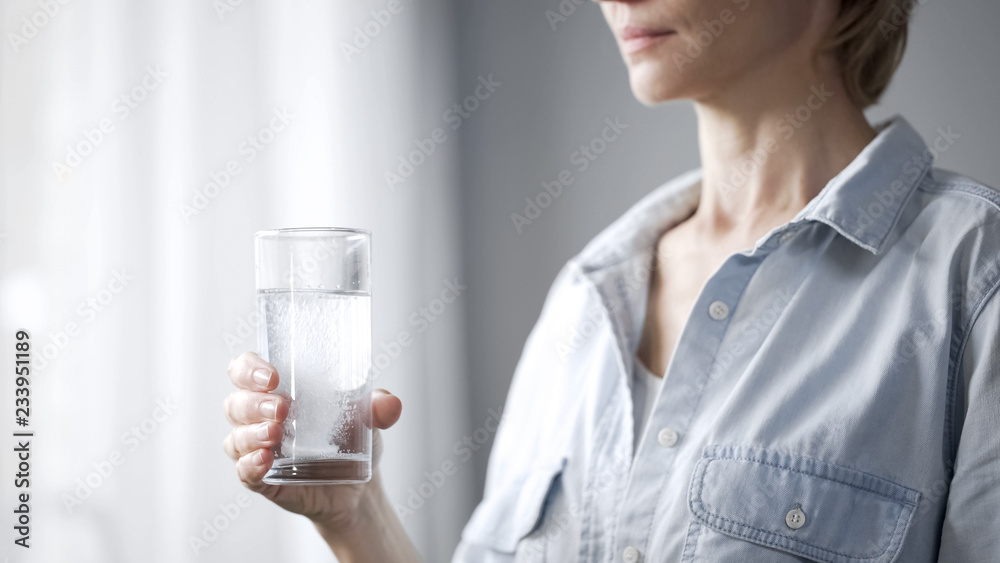 Female putting pill into glass with water, womans health, medication closeup Female putting pill into glass with water, womans health, medication closeup