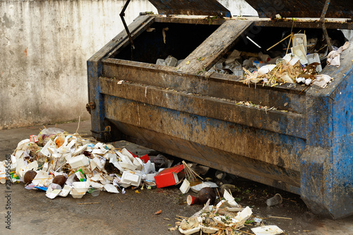 Pile of garbage outside full, disgusting, corroded trash container. Sample of incivility of people.