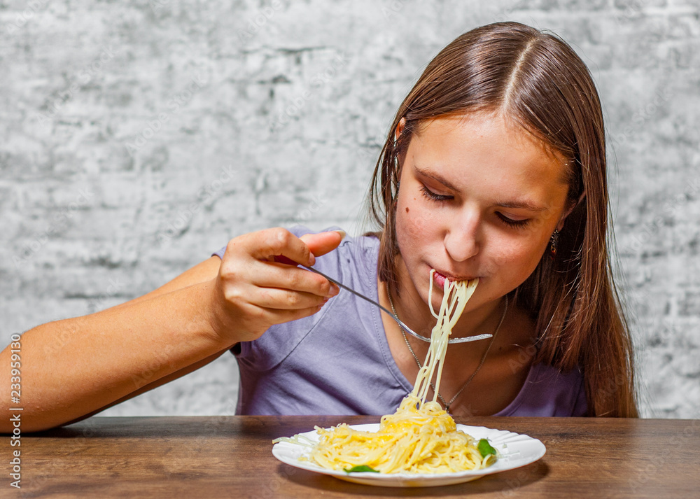 portrait of young teenager brunette girl with long hair Eating Spaghetti pasta with cheese on gray wall background portrait of young teenager brunette girl with long hair Eating Spaghetti pasta with cheese on gray wall background