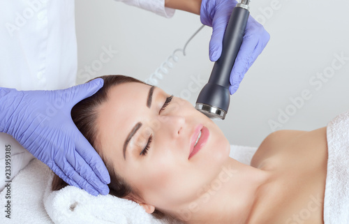 The cosmetologist makes the ultrasonic cleaning procedure of the facial skin of a beautiful woman in a beauty salon.Cosmetology and professional skin care.