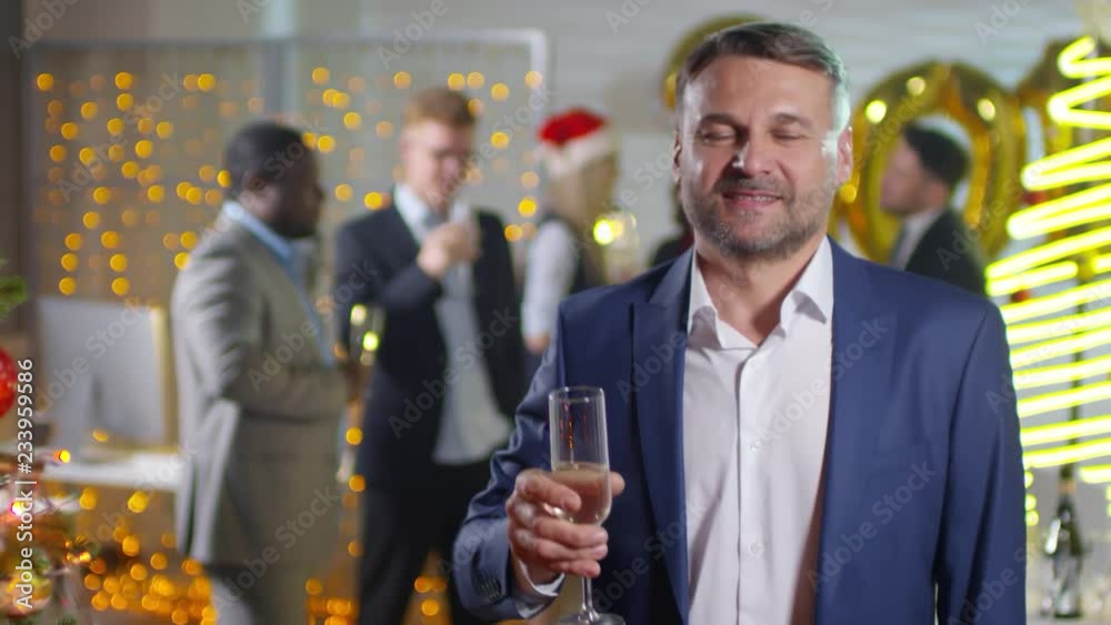 Portrait shot of cheerful businessman in suit smiling for camera and toasting with glass of champagne at Christmas party in office Portrait shot of cheerful businessman in suit smiling for camera and toasting with glass of champagne at Christmas party in office