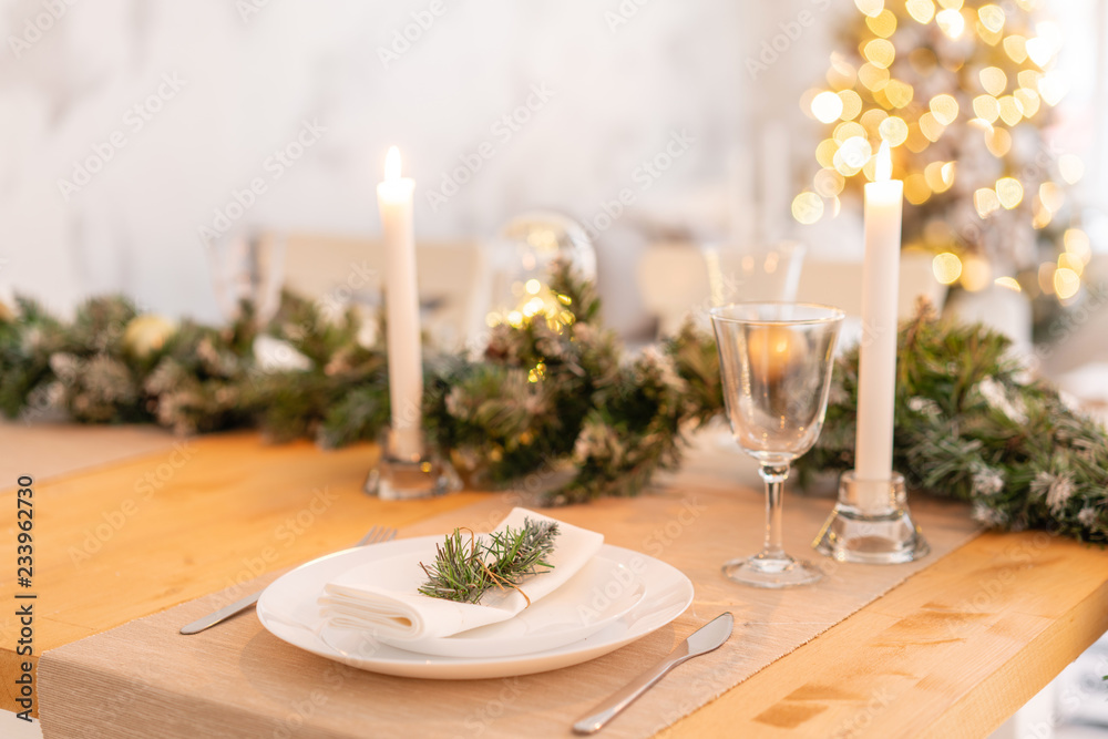 Christmas table setting. Beautiful served table with decorations, candles and lanterns. Living room decorated with lights and Christmas tree.