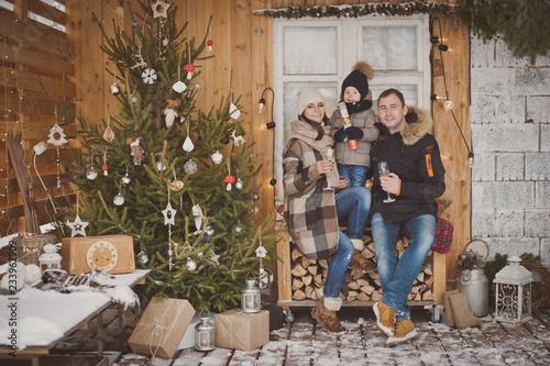Russian young family enjoying their holiday time together, decorating Christmas tree outdoors in warm clothes, arranging the christmas lights and having fun. mother father and son meet new year © shangarey