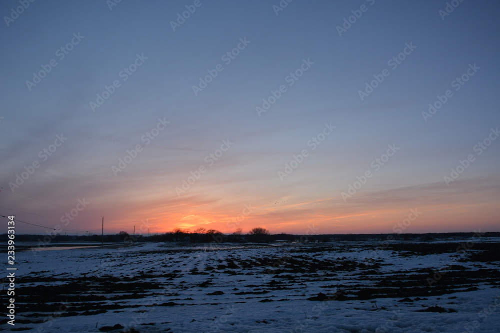 The end of a cold winters day with the sun behind the horizon and snow covered farm fields resting for the off season. 