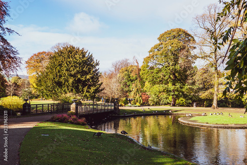 Lovely view of Buxton Park in Autumn  showing the calm pond and beautiful autumnal trees as well as the stone architecture of the town.