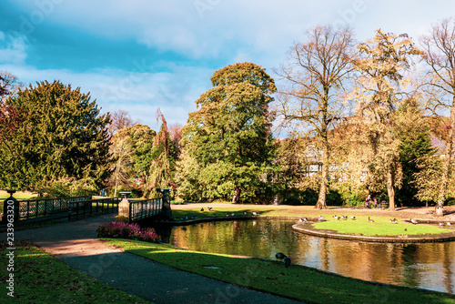 Lovely view of Buxton Park in Autumn  showing the calm pond and beautiful autumnal trees as well as the stone architecture of the town.