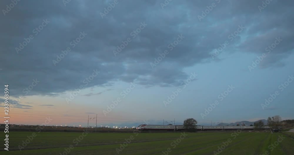 Treno alta velocità transita sotto un cielo nuvoloso al tramonto in partenza dalla stazione Treno alta velocità transita sotto un cielo nuvoloso al tramonto in partenza dalla stazione