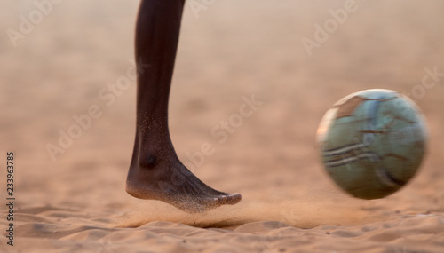 Kids playing football barefoot on sand