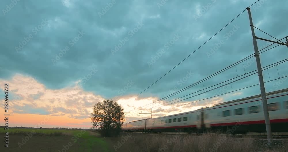 White and red passenger high speed train is departing from the station over a cloudy sky at sunset. White and red passenger high speed train is departing from the station over a cloudy sky at sunset.