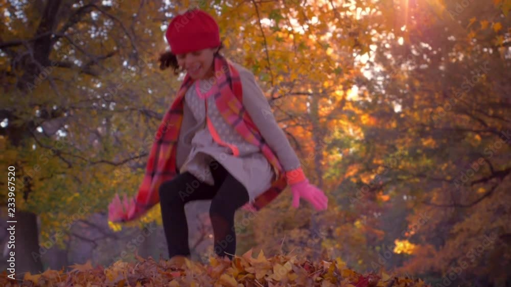 Girl jumping into a pile of leaves, filmed in slow motion