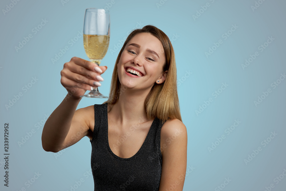 Cheerful happy young woman laughs cheerfully and raises a glass of champagne for luck and success. Studio portrait on blue background Cheerful happy young woman laughs cheerfully and raises a glass of champagne for luck and success. Studio portrait on blue background