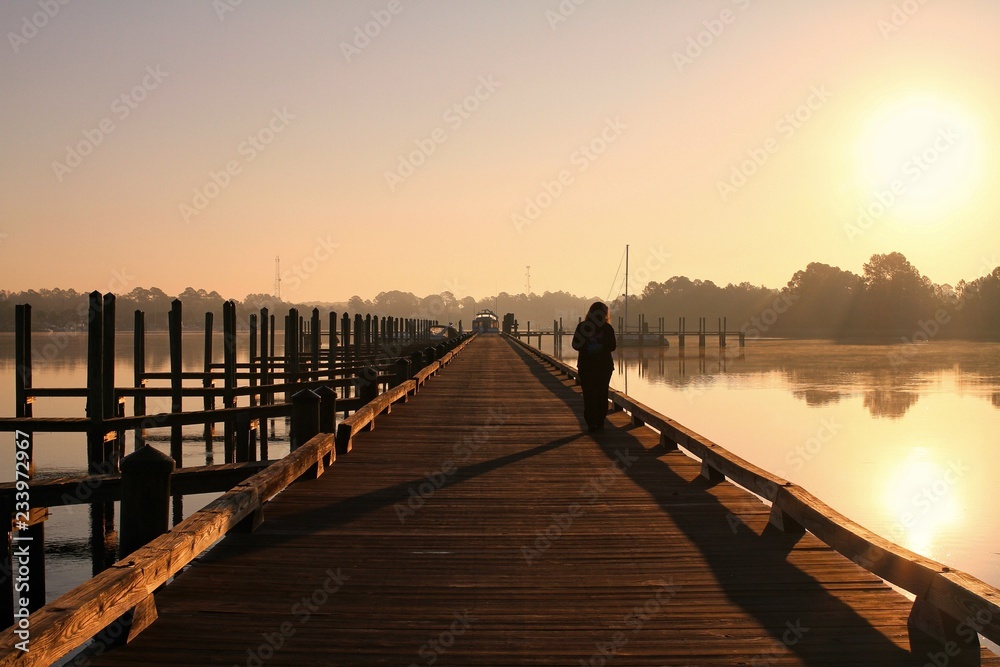 Silhouette of a woman walking on a pier at sunrise.