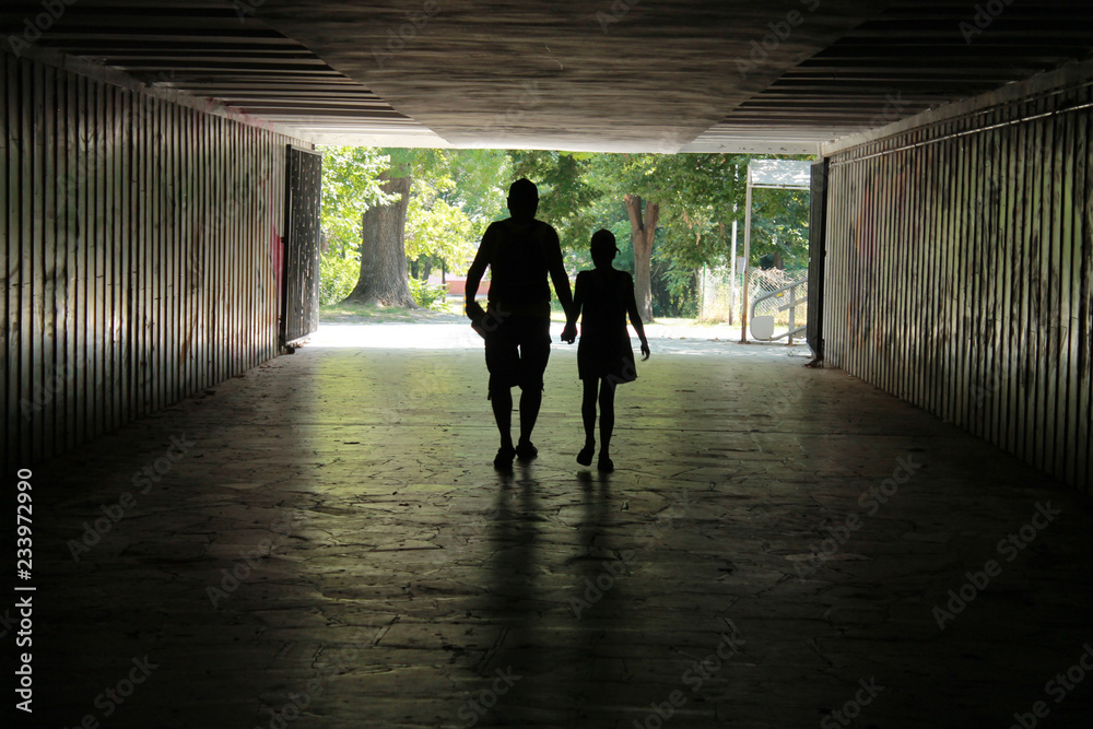 Silhouette of a man with a child in a dark tunnel, view from afar