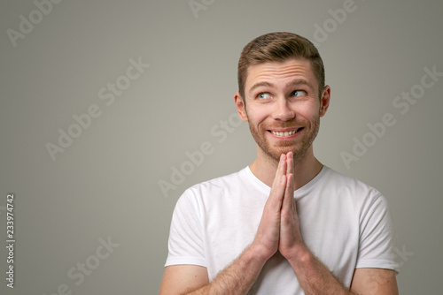 The bearded man holds hands together as if in prayer, begging for money, looking to the left with great desire. The boyfriend asks for a favor, makes a gesture of request, stands on white background
