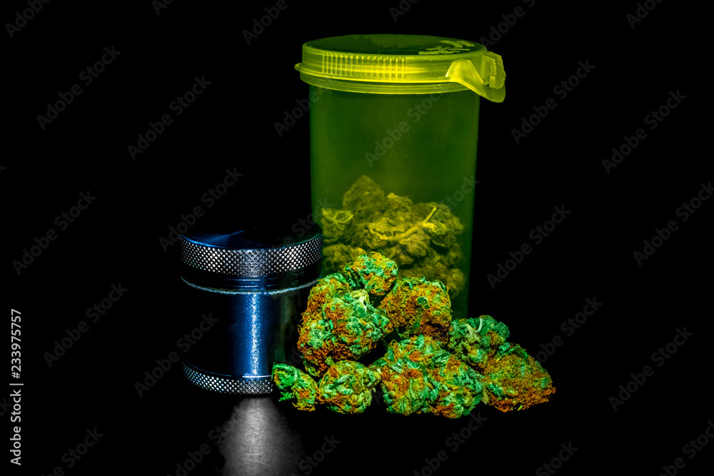 A bright green RX bottle with marijuana inside it, a pile of marijuana buds infront & a bud grinder to the left.