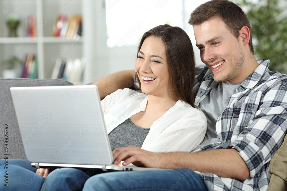 Couple checking online content in a laptop sitting at home Couple checking online content in a laptop sitting at home