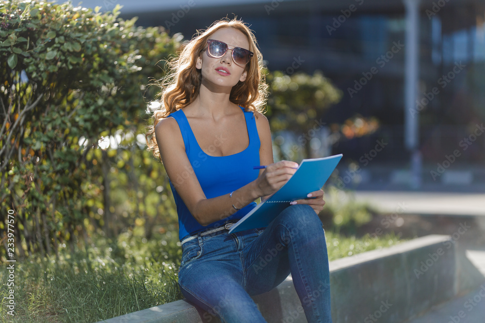 Obraz premium beautiful young girl holding a notebook in her hands on the street. concept of business or education lifestyle