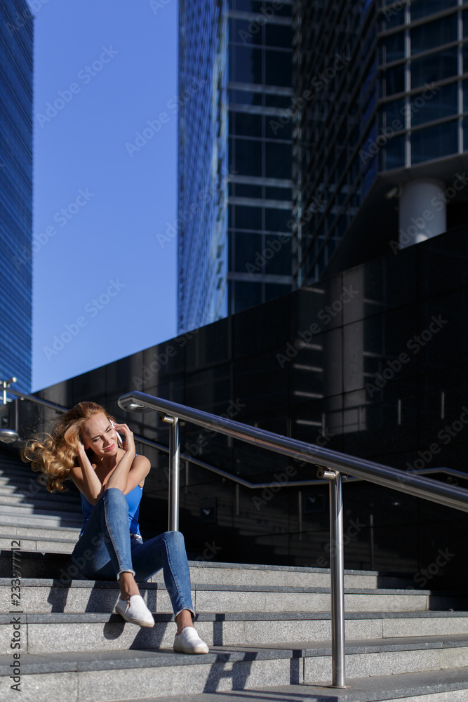Beautiful girl sitting on the steps with her smartphone between skyscrapers