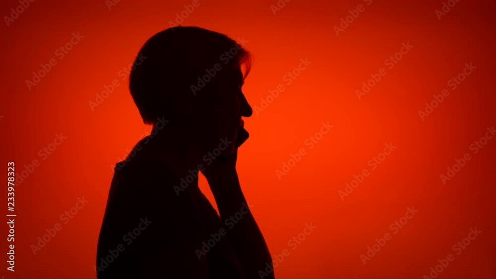 Silhouette of senior woman using mobile on red background. Female's face in profile talking on cellphone. Black contur shadow of grandmother's half-face Silhouette of senior woman using mobile on red background. Female's face in profile talking on cellphone. Black contur shadow of grandmother's half-face