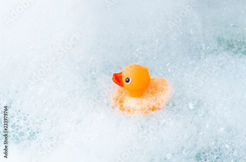 Orange playful rubber duck on the edge of the bath, blue bubble background. Children's washing concept. Children`s pool area concept. Room for text. photo